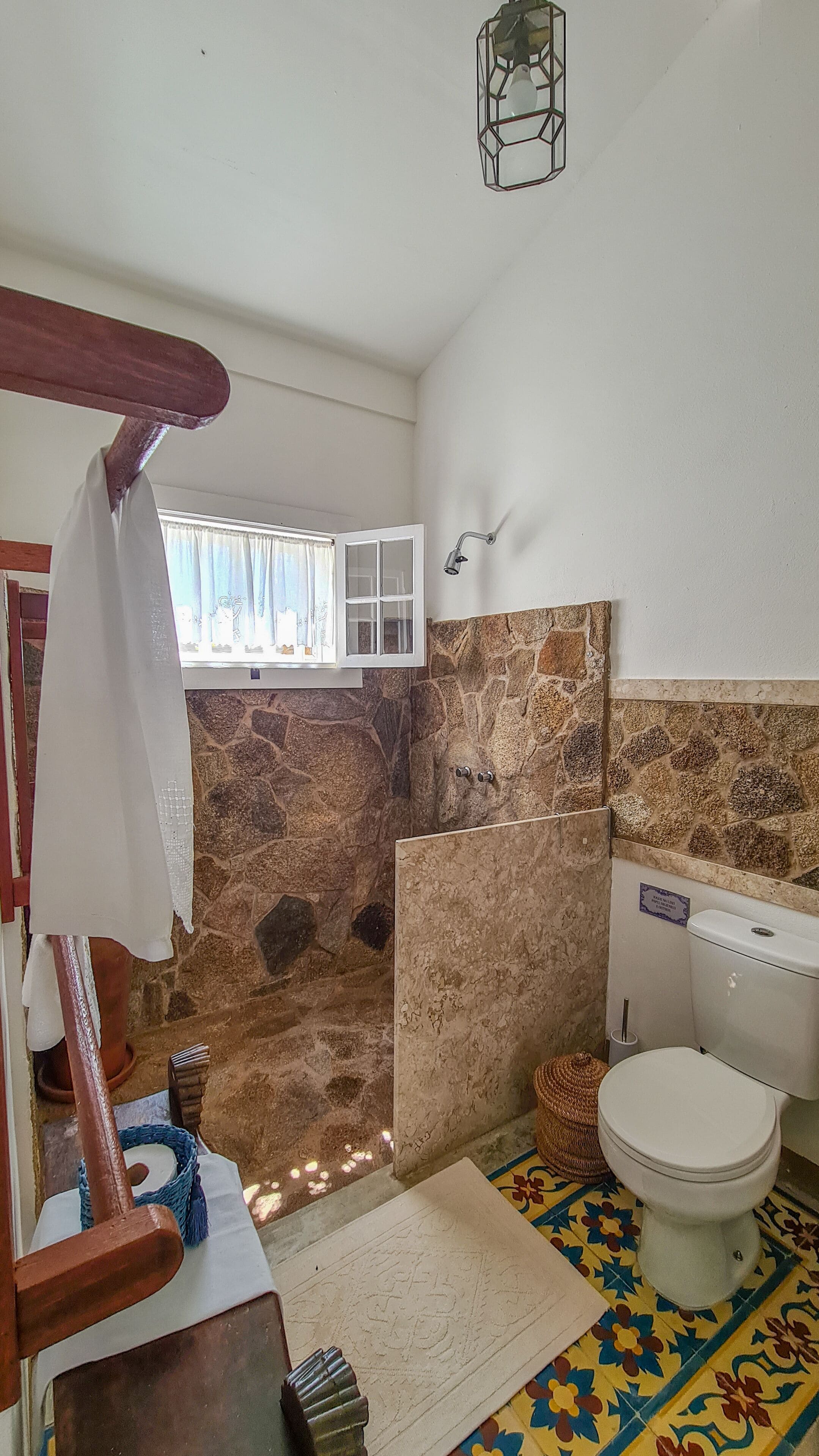 A bathroom with a stone wall, a window, a toilet, and a shower area.