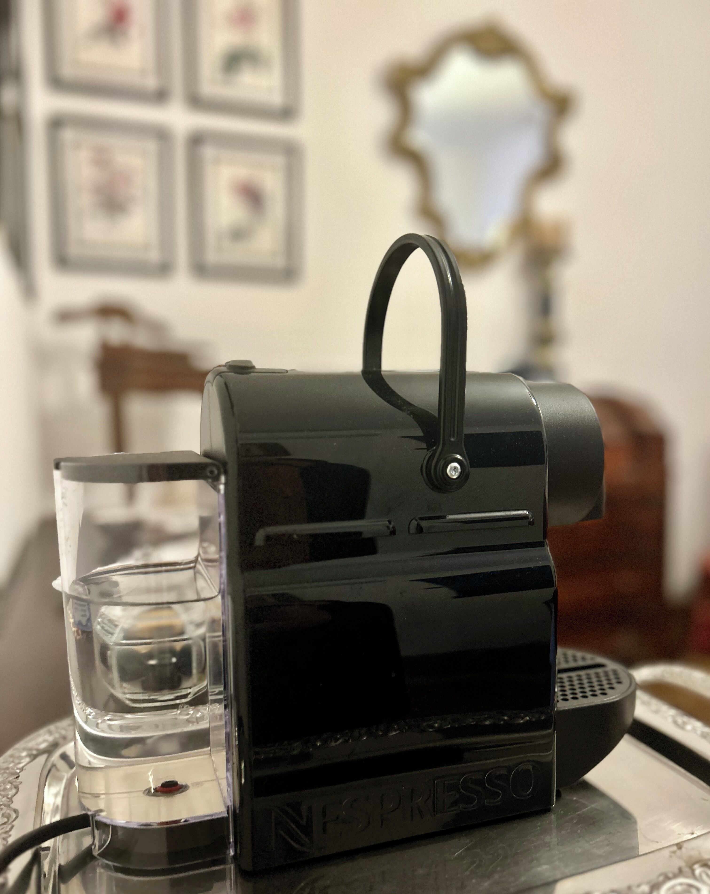 Une machine à café Nespresso avec un verre d’eau posé sur une table.