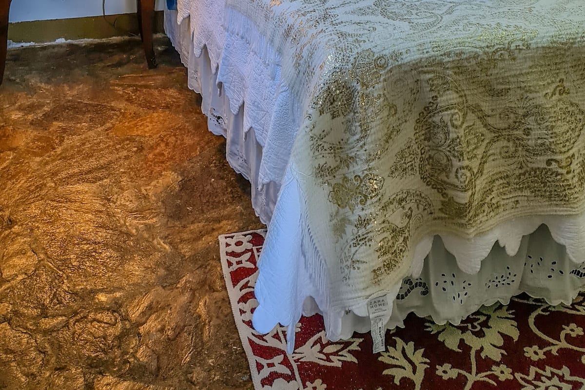 A neatly made bed with white linens and a decorative headboard, a bedside table with a lamp, and a large framed painting on the wall.