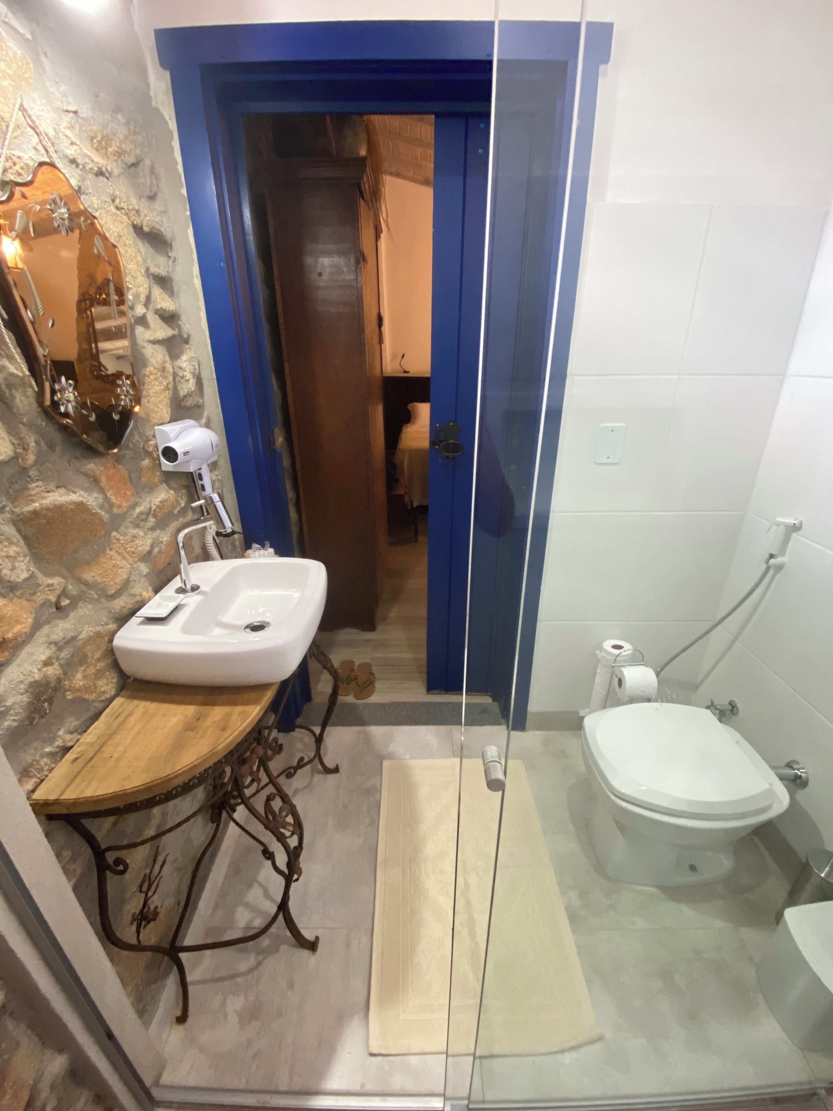 A bathroom with a stone wall, a wooden vanity, a white sink, a glass shower enclosure, and a toilet.