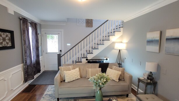 A living room with a sofa, a coffee table, a vase with flowers, a lamp, and a staircase leading to another room. - Spacious, Fully-Stocked, Walking distance to Downtown - With Comfy Mattresses! (Bardstown)