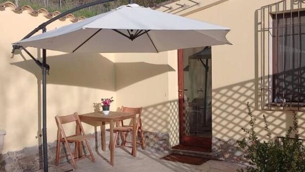 An outdoor patio with a table and chairs, a white umbrella, and a door with a metal gate. - La Ginestra, vacation home in the mountains(Seulo Sardinia)garden wonderful view  (Seulo)