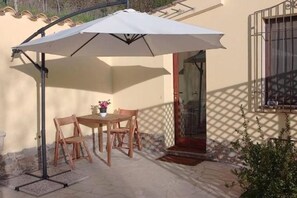 An outdoor patio with a table and chairs, a white umbrella, and a door with a metal gate. - La Ginestra, vacation home in the mountains(Seulo Sardinia)garden wonderful view  (Seulo)