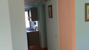 A narrow hallway with light blue walls and a tiled floor leading to a kitchen area with cabinets and a stove. - La Ginestra, vacation home in the mountains(Seulo Sardinia)garden wonderful view  (Seulo)