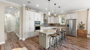 Una cocina moderna con armarios blancos, electrodomésticos de acero inoxidable y una isla central con taburetes de bar.