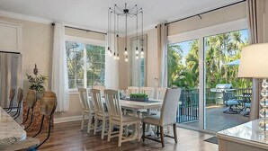 Un comedor con mesa y sillas de madera, una araña y vistas a una terraza con mobiliario exterior.