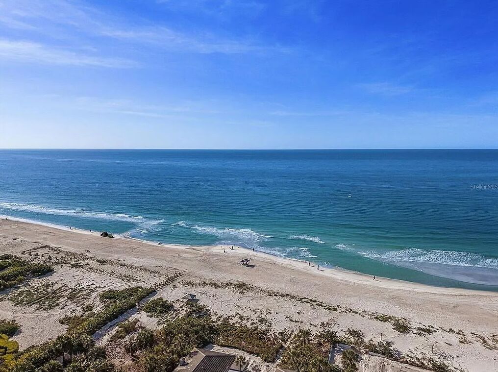 Een strand met helderblauw water, een zandstrand en weinig begroeiing.