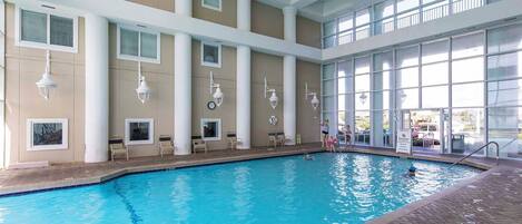 An indoor swimming pool with clear blue water, surrounded by a tiled floor and a brick border.