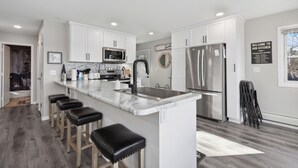 Una cocina moderna con gabinetes blancos, electrodomésticos de acero inoxidable y una isla de mármol con taburetes de bar.