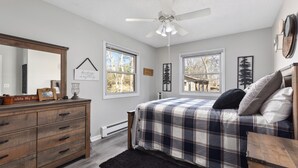Un dormitorio con cama, cómoda y ventilador de techo. Hay ventanas y cuadros en la pared.