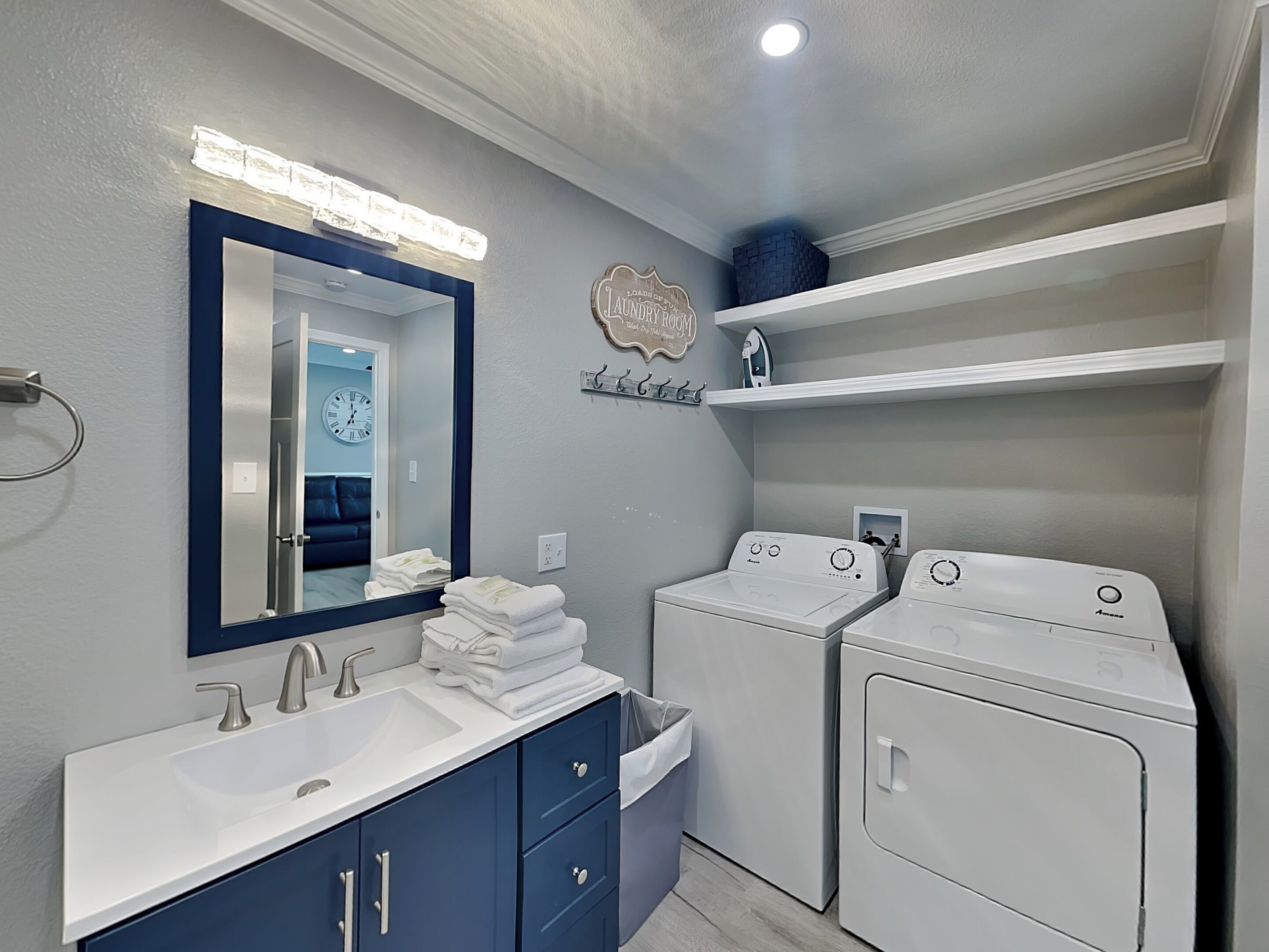 A bathroom with a large mirror, two washing machines, a sink, and a towel rack.