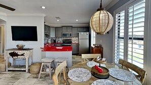 A modern kitchen with a red island, a dining area with patterned tableware, and a large window with blinds. - Paradise Isle #15A by Southern Vacation Rentals (Gulf Shores)