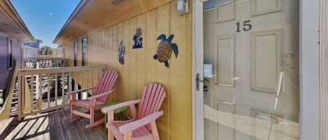 A wooden deck with two Adirondack chairs, a small table, and a door marked with the number 15.