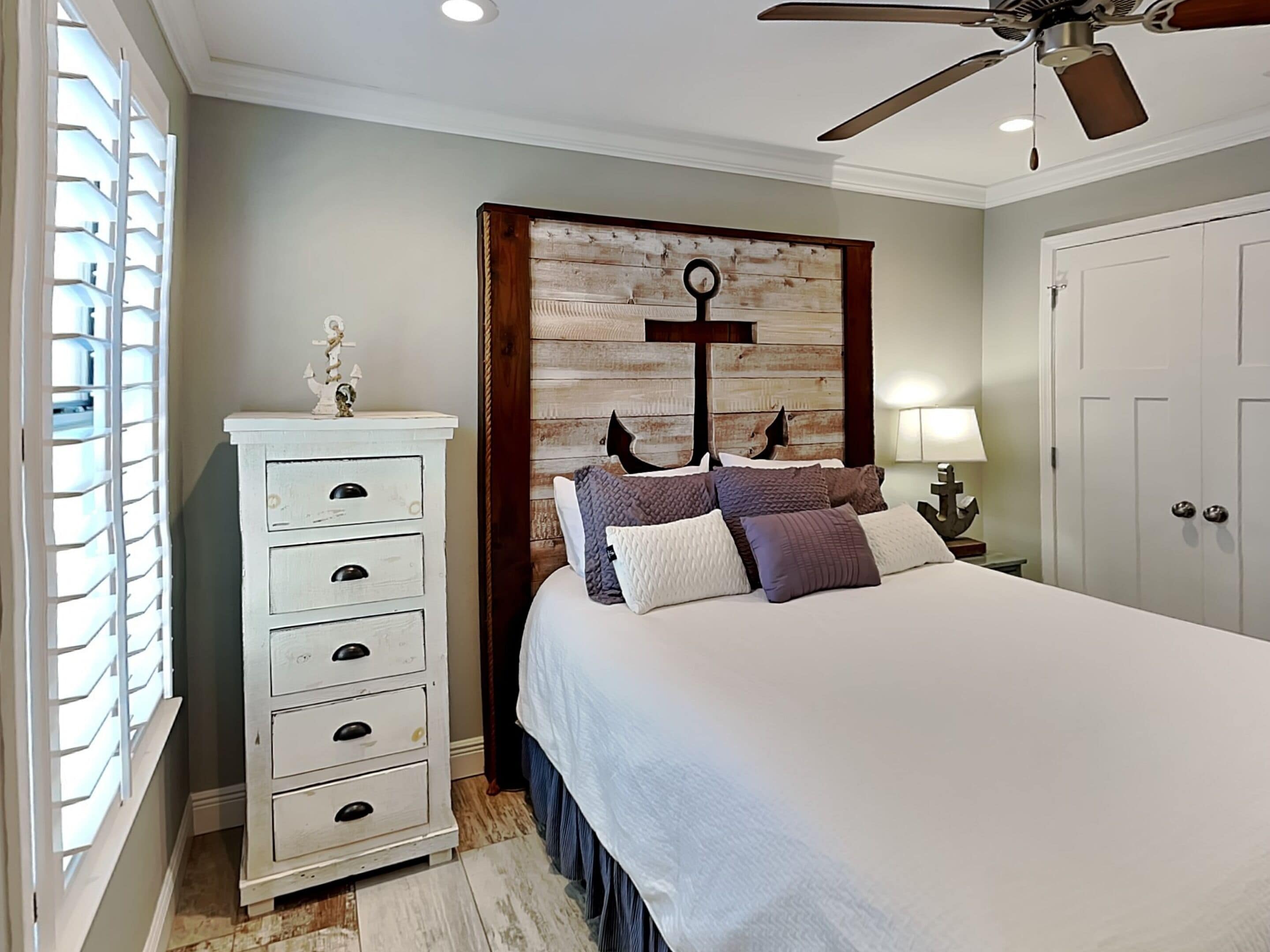 A bedroom with a bed, a dresser, a wall-mounted cross, and a ceiling fan.