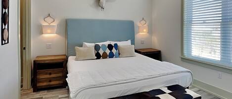 Un dormitorio con una cama grande, cabecera con cráneo de vaca, dos mesitas de noche, un banco y una ventana con persianas.