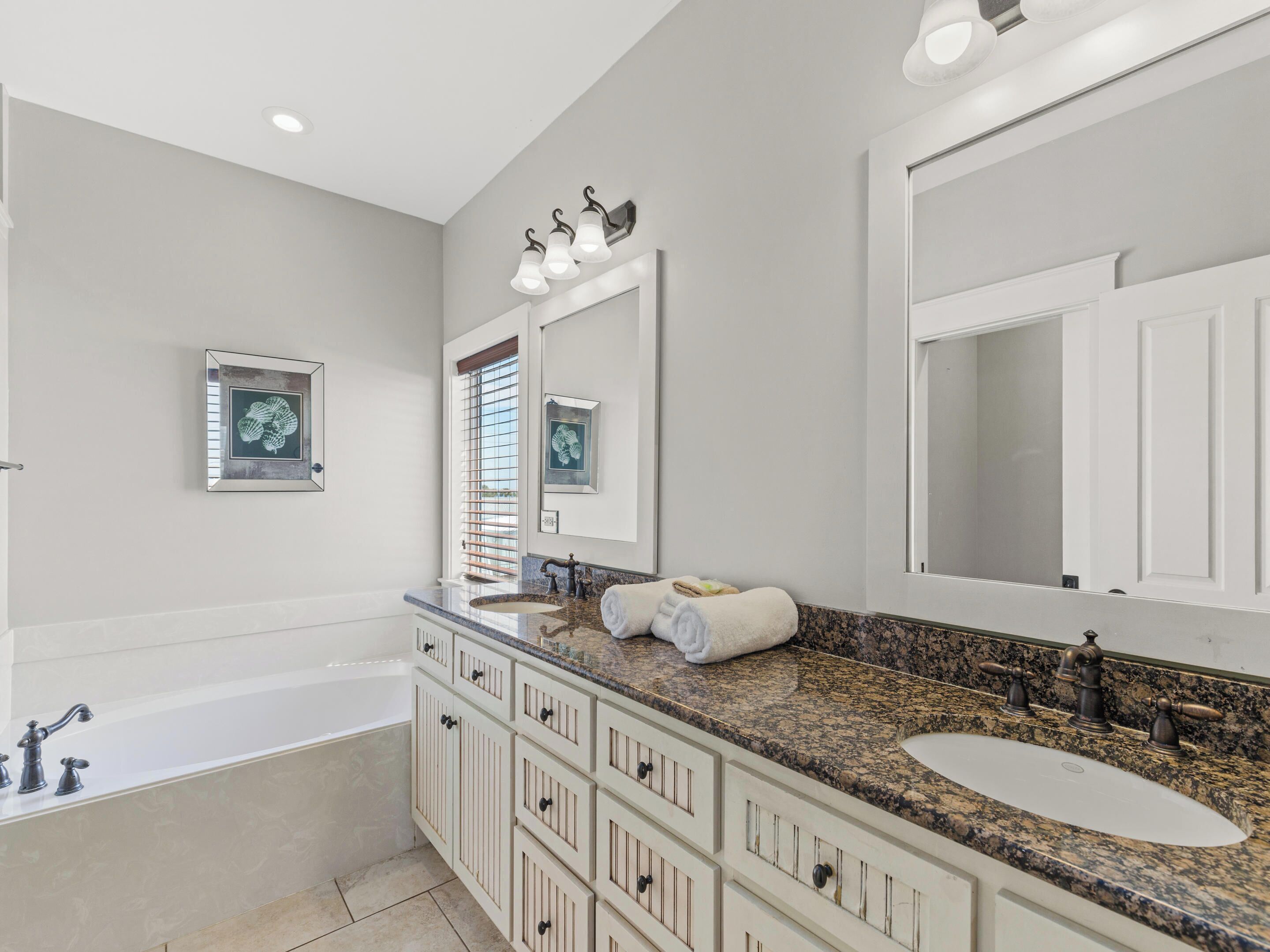 A modern bathroom with a bathtub, a sink, and a vanity with drawers. There are three wall-mounted lights above the vanity and a large mirror above the sink.