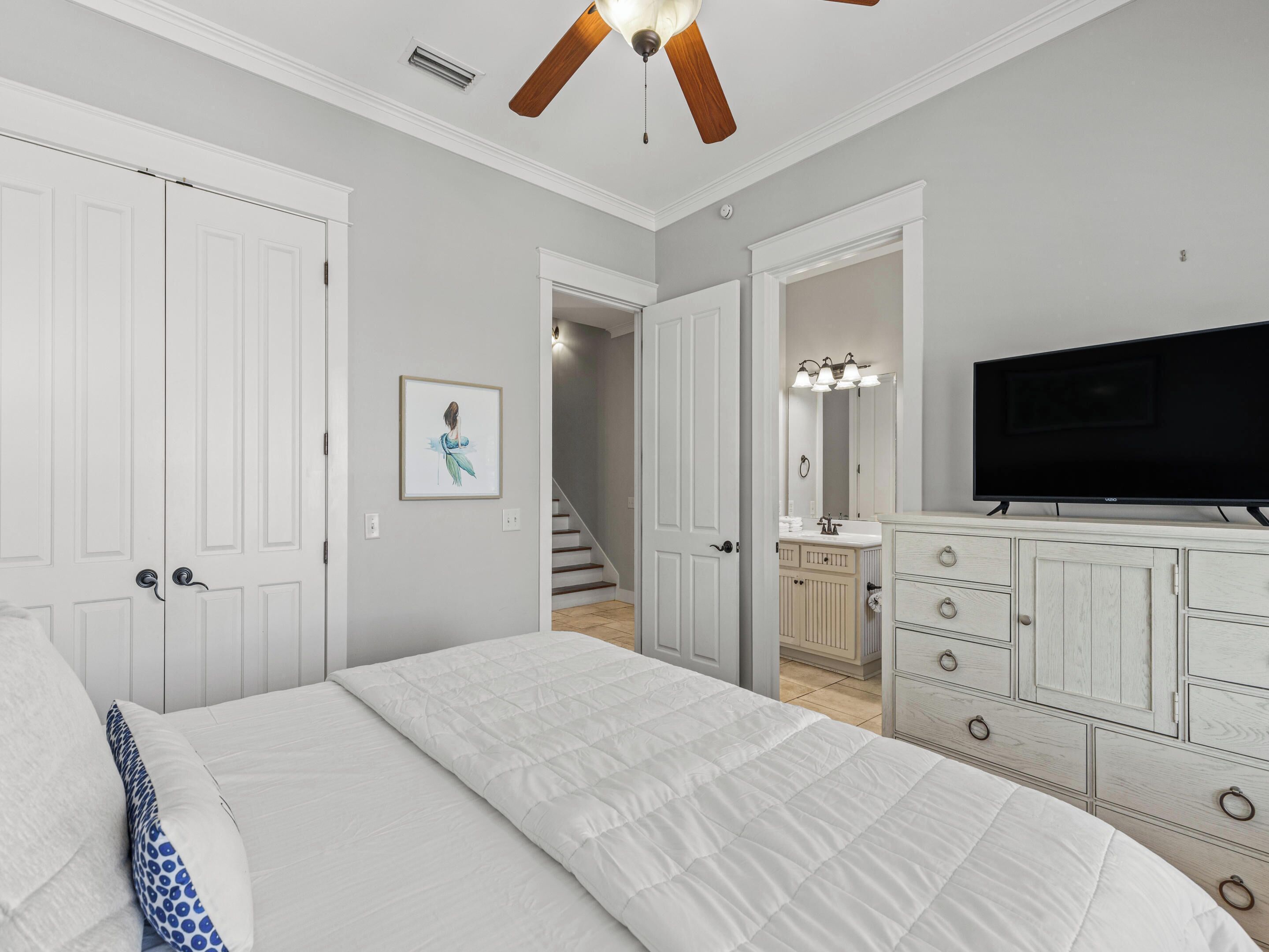 A bedroom with a bed, dresser, TV, and a staircase leading to a bathroom.