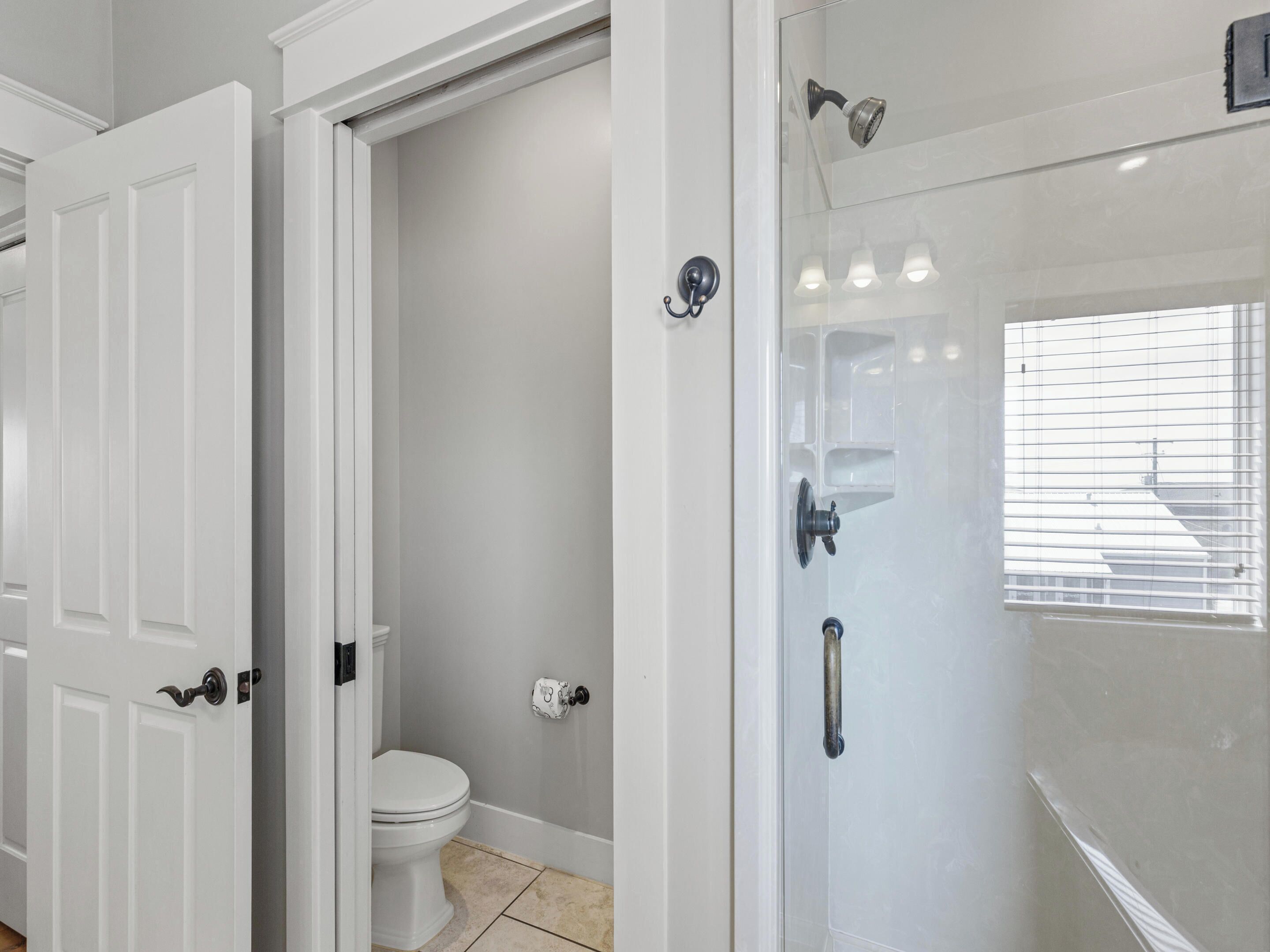 A bathroom with a toilet, a shower with a glass door, and a window with blinds.