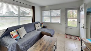 A modern living room with a grey sofa, a wooden coffee table, and a door leading outside. - Seashell Cottage by Resort Collection (Panama City Beach)