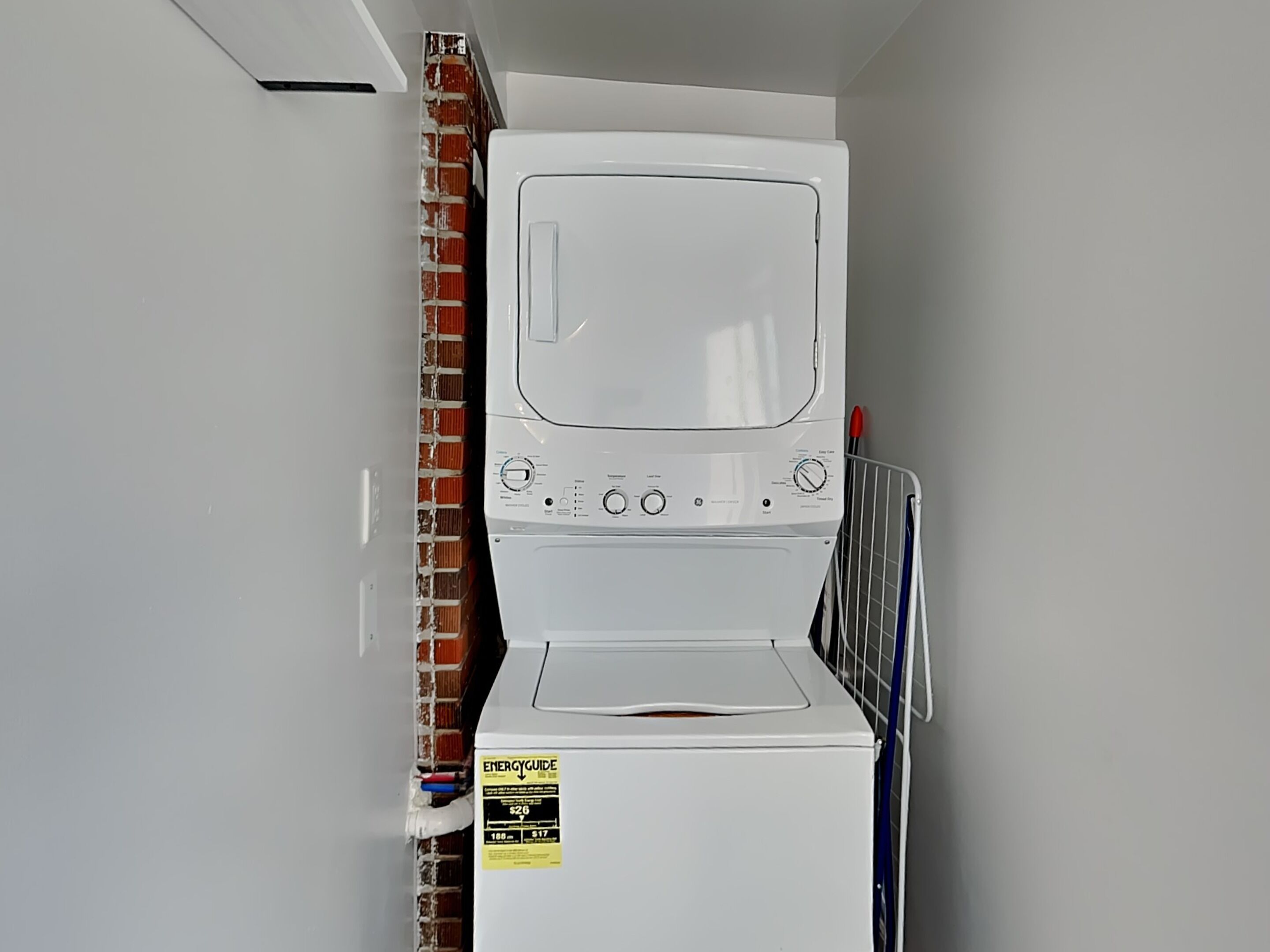 A white washer and dryer unit with an ENERGYGUIDE sticker, a metal rack, and a brick wall.