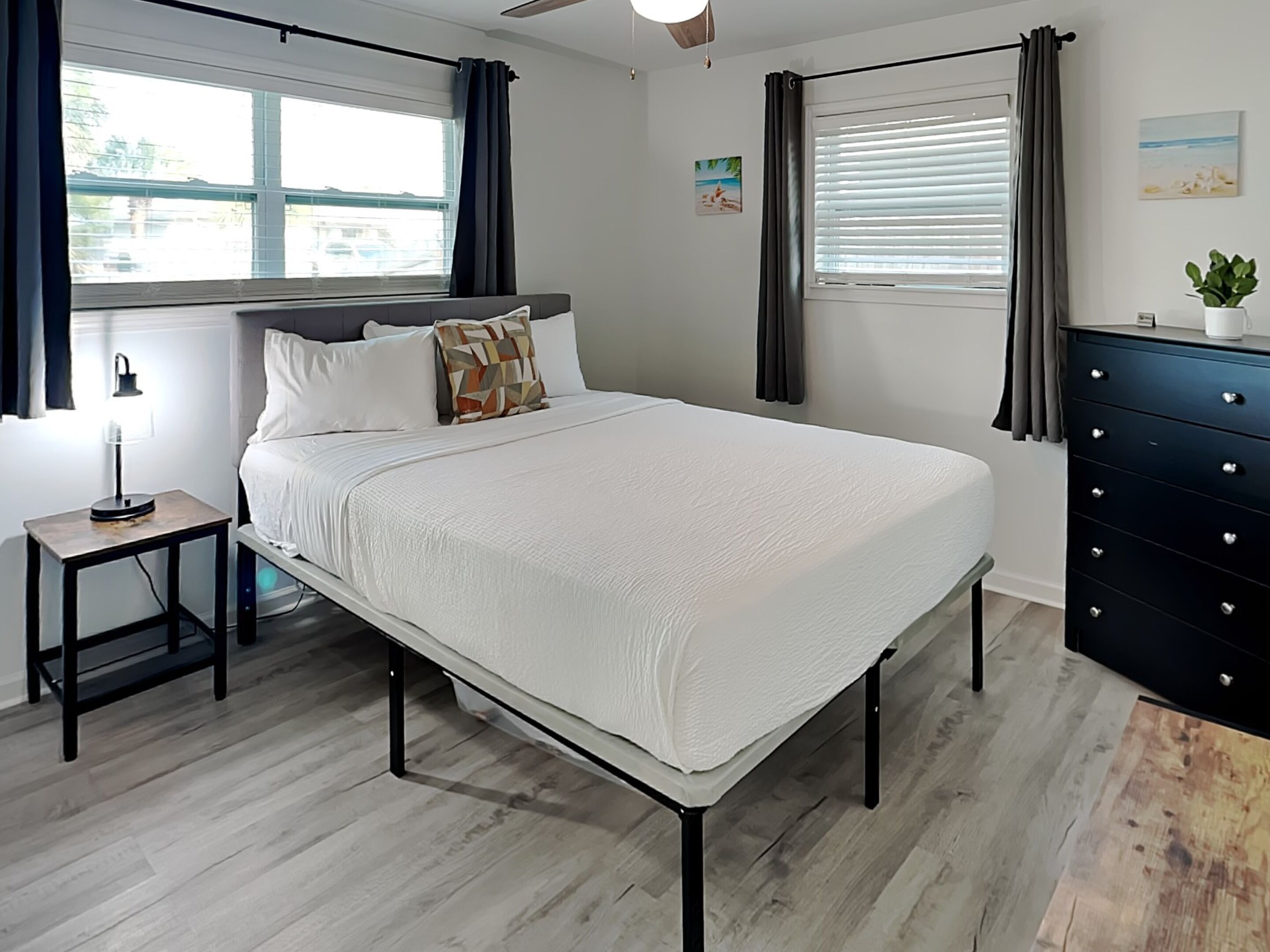 Une chambre à coucher moderne avec un grand lit, une table de chevet avec une lampe, une commode et une fenêtre avec des rideaux.