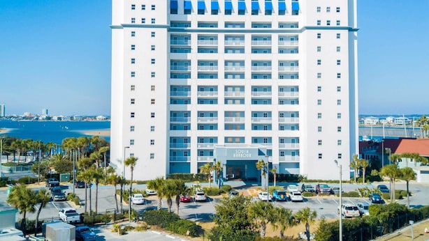 A multi-story hotel with a central entrance, parking lot, and a view of the ocean. - South Harbour #2F by Southern Vacation Rentals (Pensacola Beach)