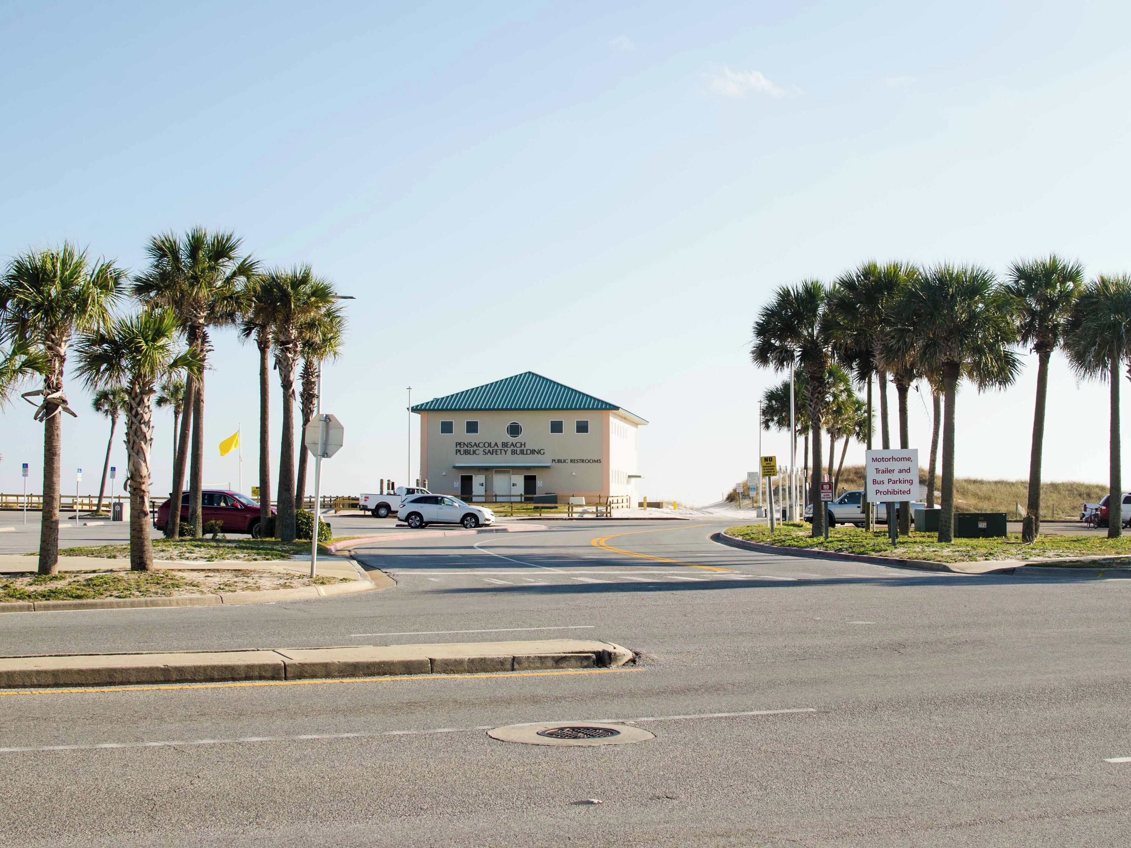 A public safety building with a green roof, located at the end of a street lined with palm trees.