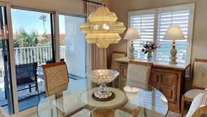 A dining area with a glass table, chairs, a chandelier, and a view of the outdoors. - South Harbour #2F by Southern Vacation Rentals (Pensacola Beach)
