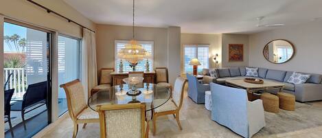 A spacious living room with a glass dining table, comfortable seating, and a large window.