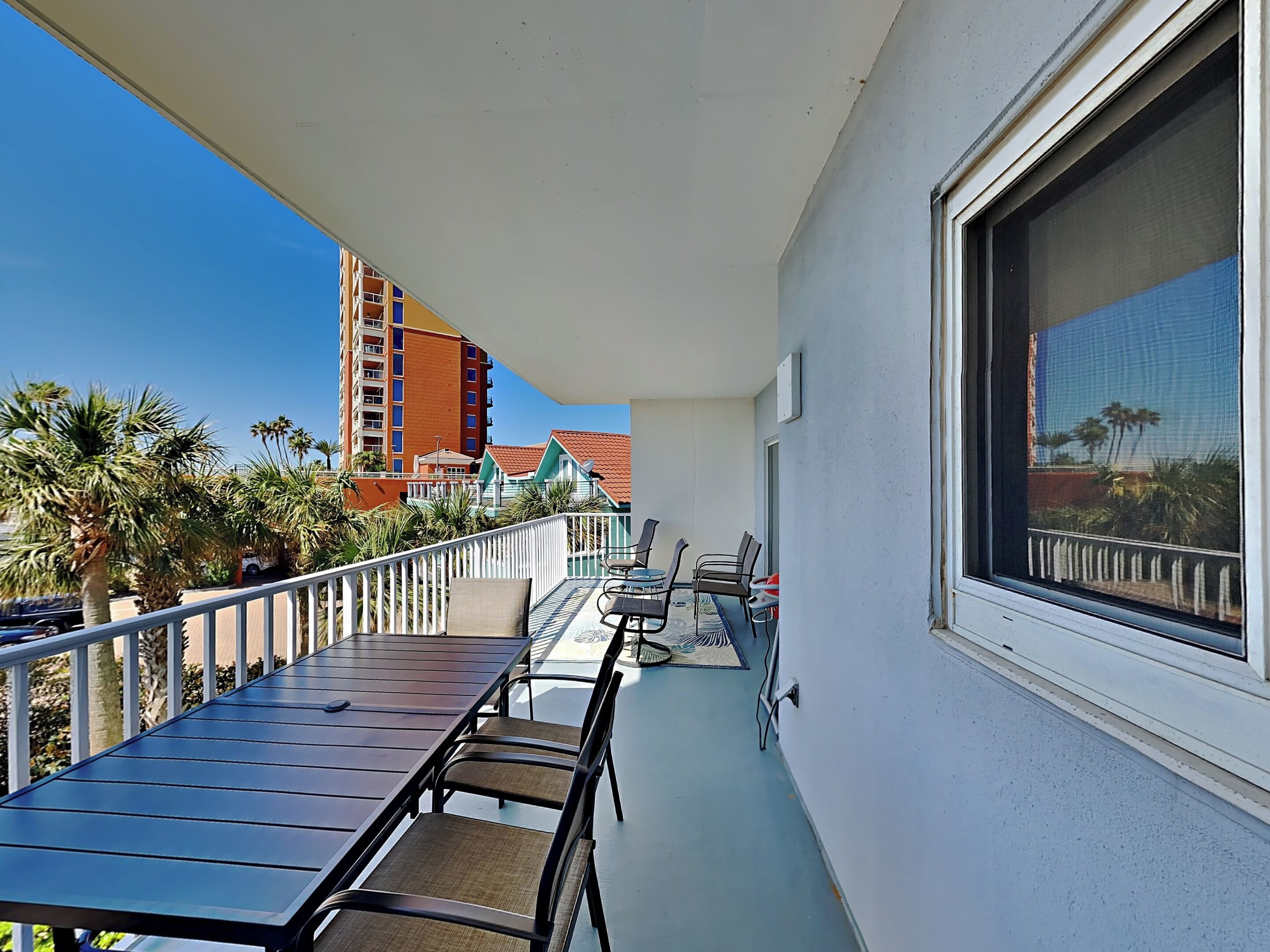 A balcony with a table and chairs, overlooking a building and palm trees.
