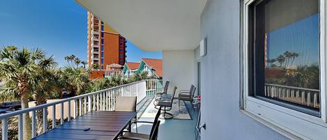 A balcony with a table and chairs, overlooking a building and palm trees.