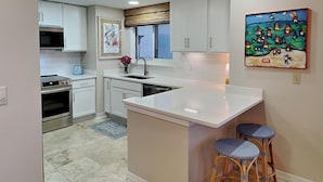 A modern kitchen with white cabinets, a central island, and two bar stools. - South Harbour #2F by Southern Vacation Rentals (Pensacola Beach)