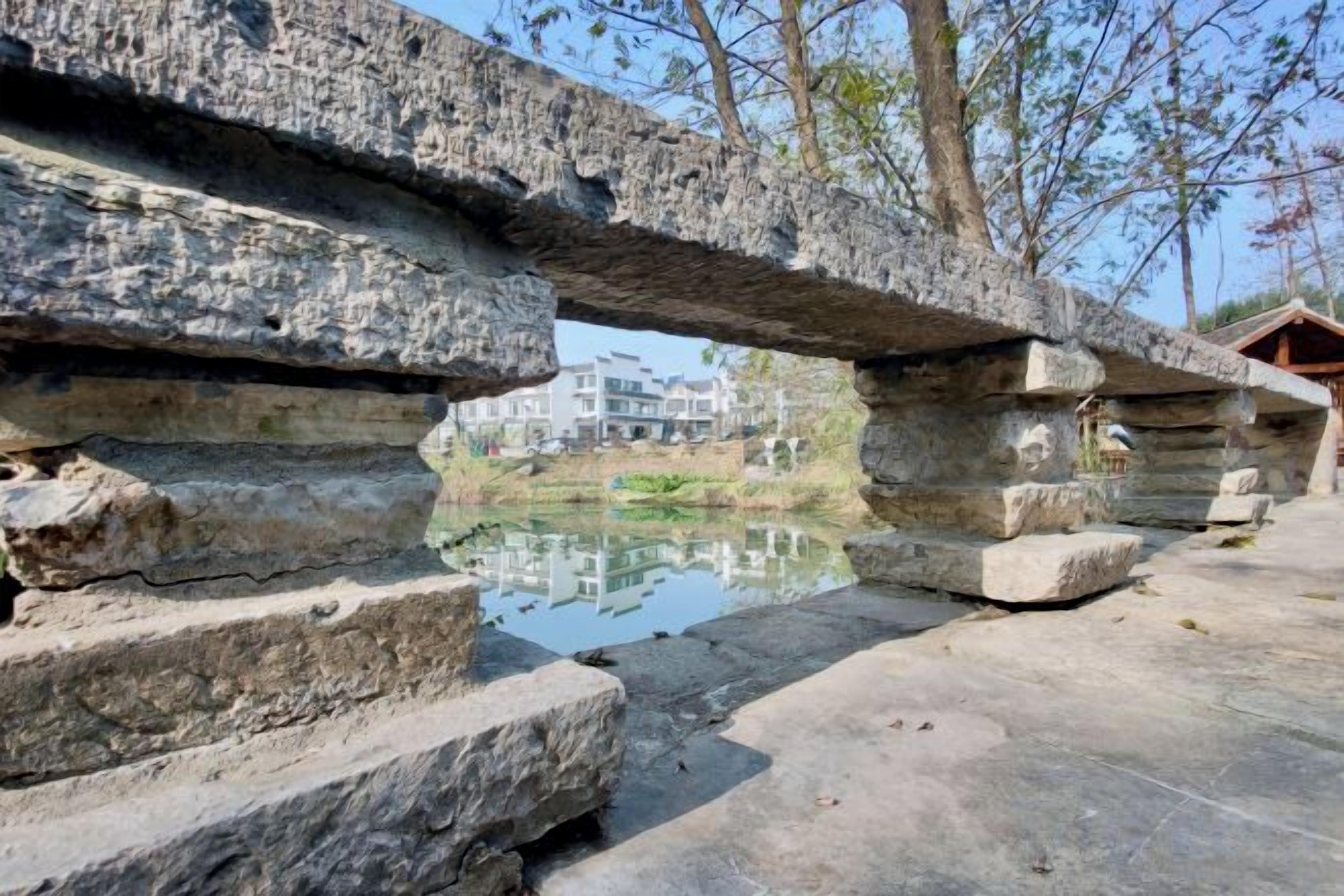 A stone bridge with a pond underneath, leading to a building with a reflection.
