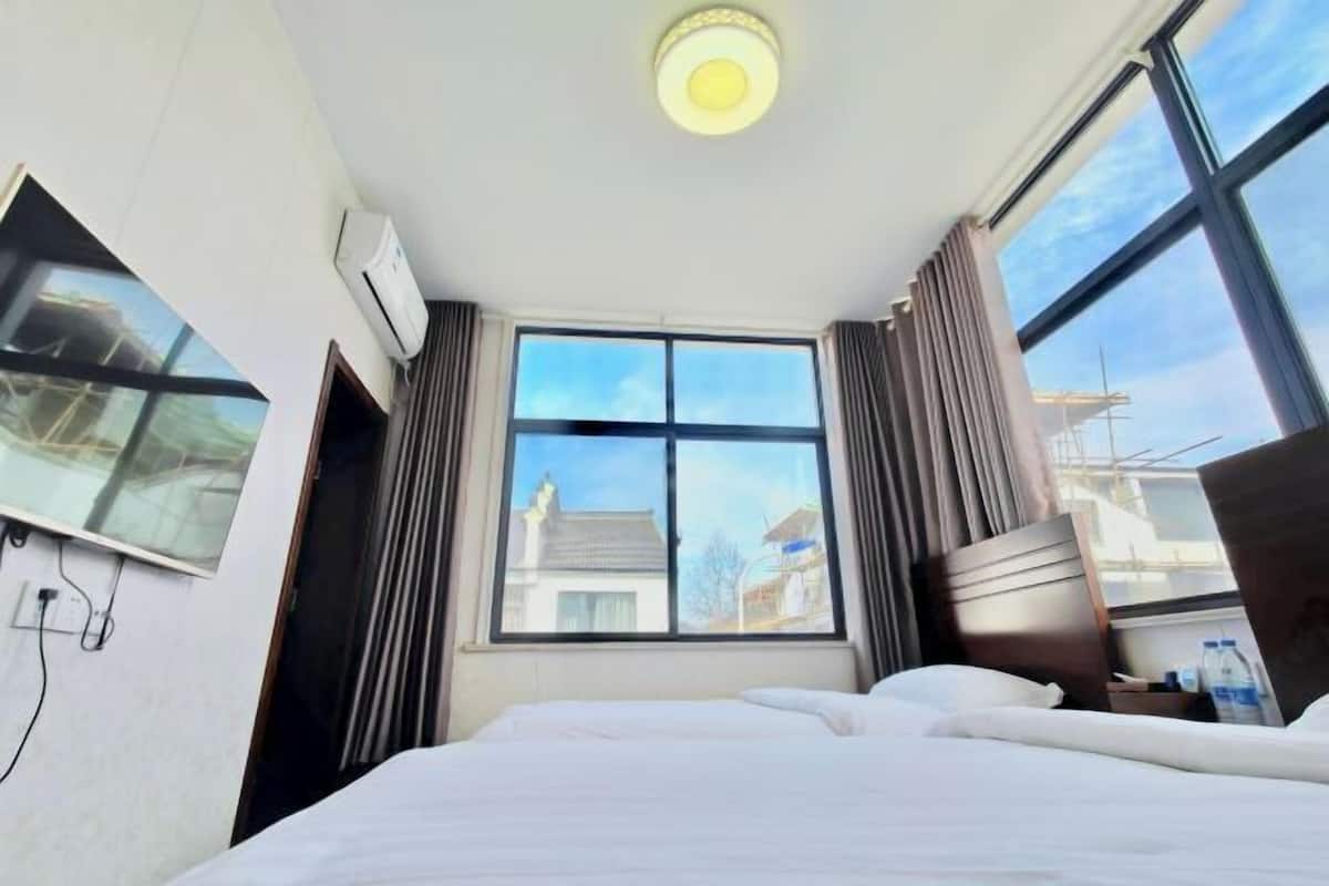 Une chambre d’hôtel avec un lit, une fenêtre avec des rideaux, un appareil de climatisation et une vue sur les bâtiments environnants.