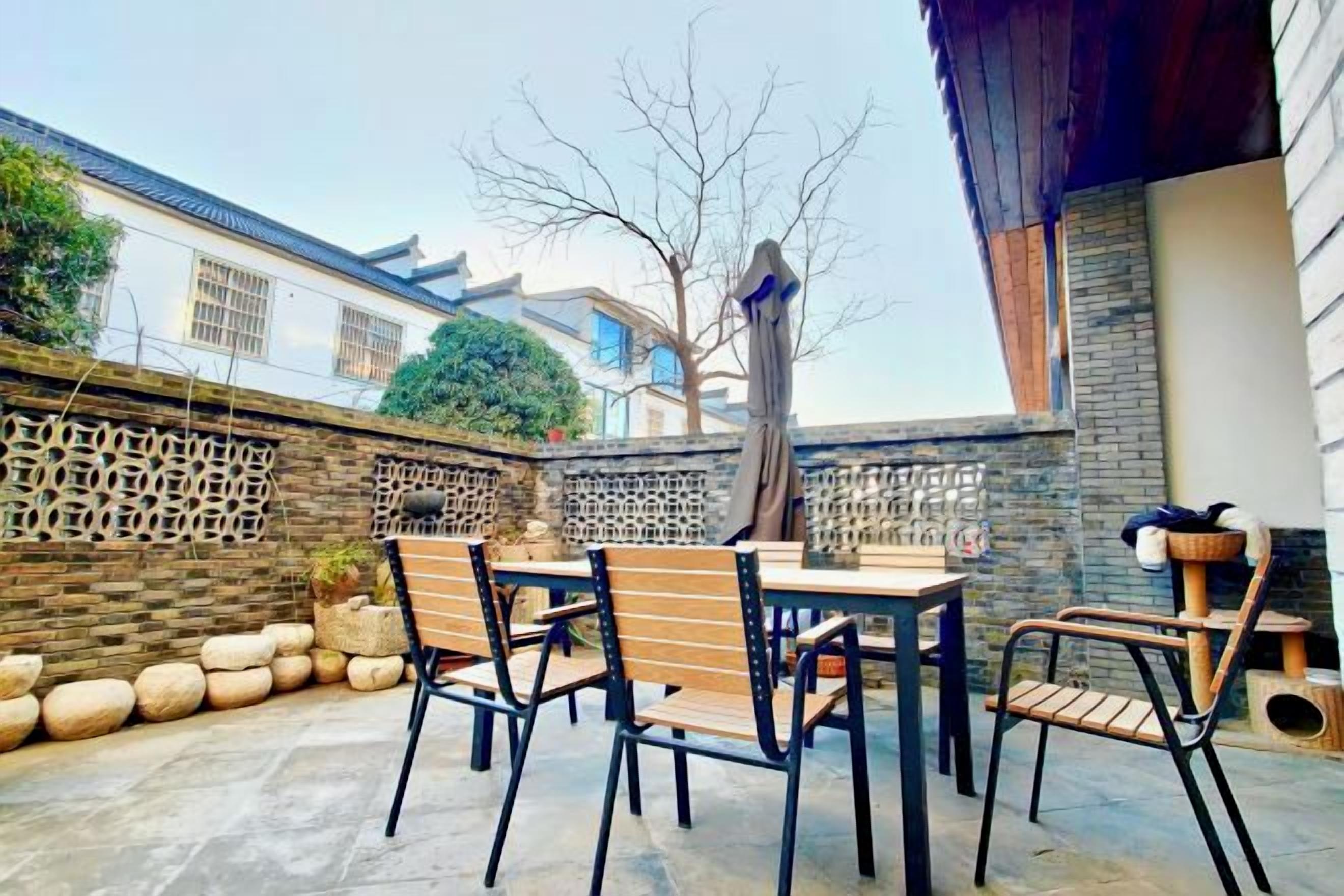 An outdoor patio with a table and chairs, a decorative wall, and a tree.