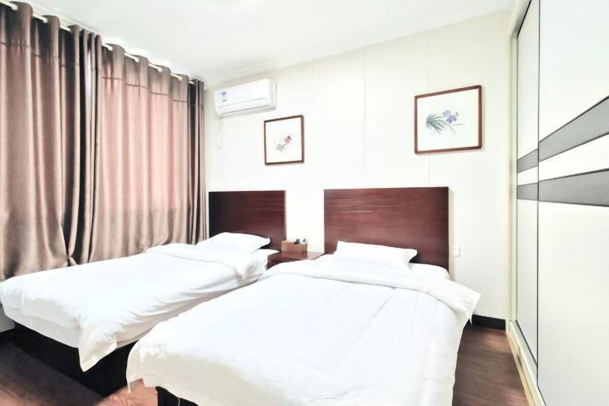 Une chambre d’hôtel avec deux lits, une tête de lit en bois, une table de chevet et un climatiseur fixé au mur.