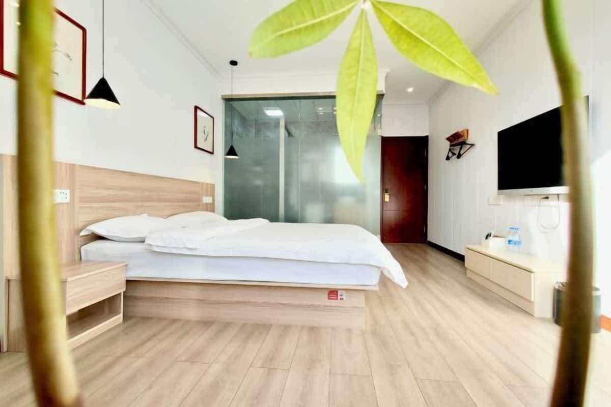 Une chambre d’hôtel moderne avec un plancher en bois, un lit avec du linge de lit blanc, une table de chevet, une télévision et une grande fenêtre.