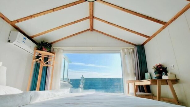 Une chambre avec un plafond en pente, un lit, une fenêtre avec des rideaux, un petit bureau et une plante.