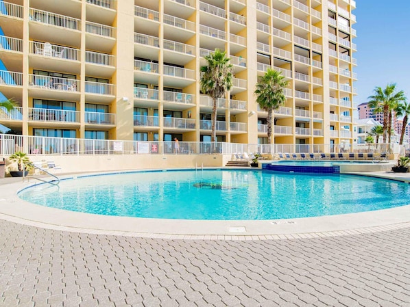 A hotel with multiple balconies, a swimming pool, and palm trees.