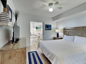 A bedroom with a large bed, a ceiling fan, a TV, and a dining area with chairs and a table.