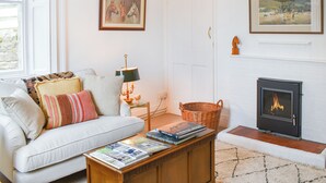 Una sala de estar con un sofá blanco, una mesa de centro con revistas, una chimenea y obras de arte enmarcadas en las paredes.