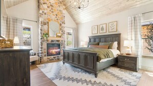 A bedroom with a stone fireplace, a bed with a dark headboard, a nightstand, and a large mirror. - Lakefront Cabin–Pool, Private Hot, Tub & Fireplace (Branson)