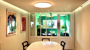 A dining area with a round table, chairs, a chandelier, and a view through a window with green curtains. - Terrasses sur la mer (Sète)