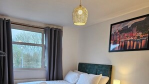 A bedroom with a bed, a nightstand, a lamp, a picture on the wall, and a window with curtains. - City Classic- Remarkable 3-bed House in Birmingham (Birmingham)