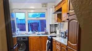 A kitchen with wooden cabinets, a washing machine, and a refrigerator. - City Classic- Remarkable 3-bed House in Birmingham (Birmingham)