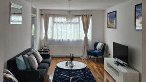 A modern living room with a dark blue sofa, a round coffee table, and a flat-screen TV on a white stand. - City Classic- Remarkable 3-bed House in Birmingham (Birmingham)