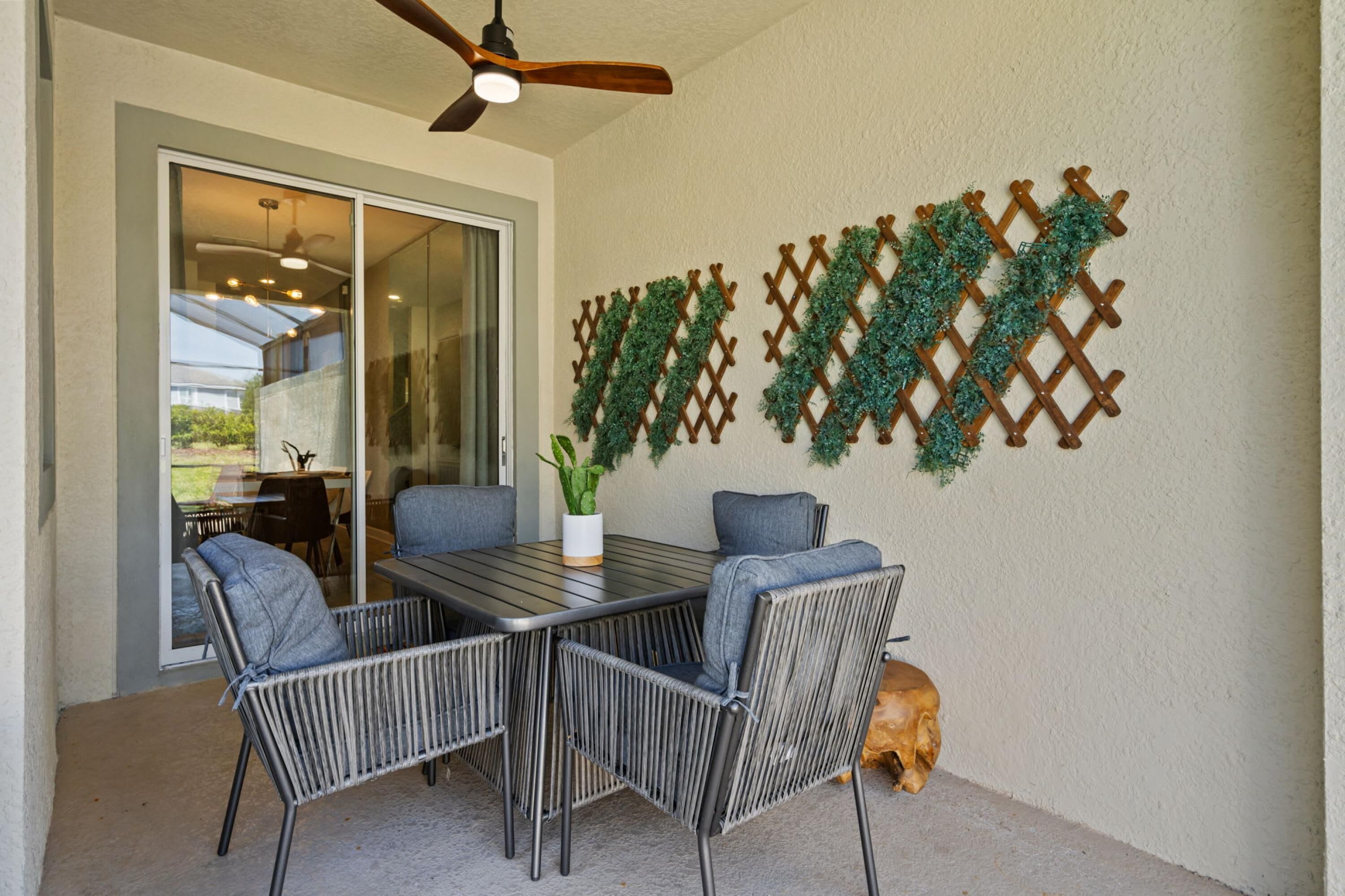 An outdoor patio with a table and chairs, a ceiling fan, and a decorative lattice wall.