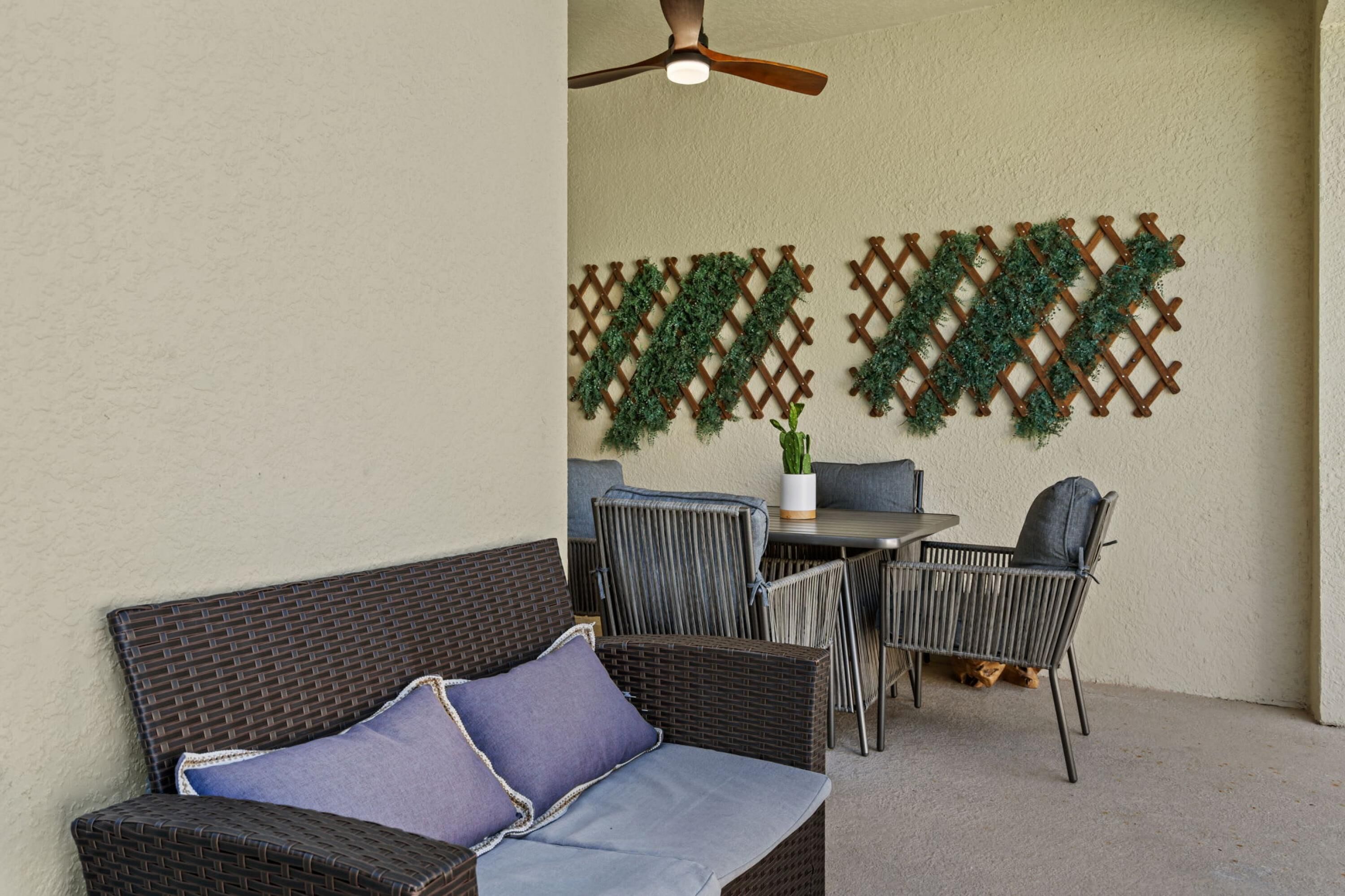 Un espace patio extérieur aménagé avec des meubles en osier, un ventilateur de plafond et des plantes décoratives fixées au mur.