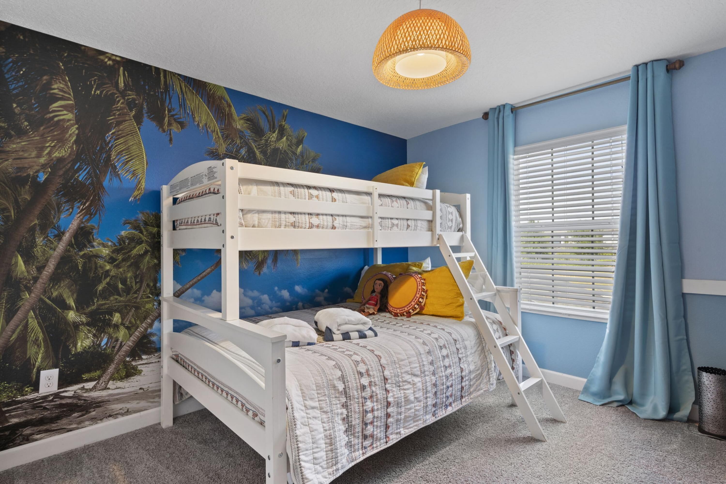 A bunk bed with a tropical mural, a ladder, and a window with blue curtains.