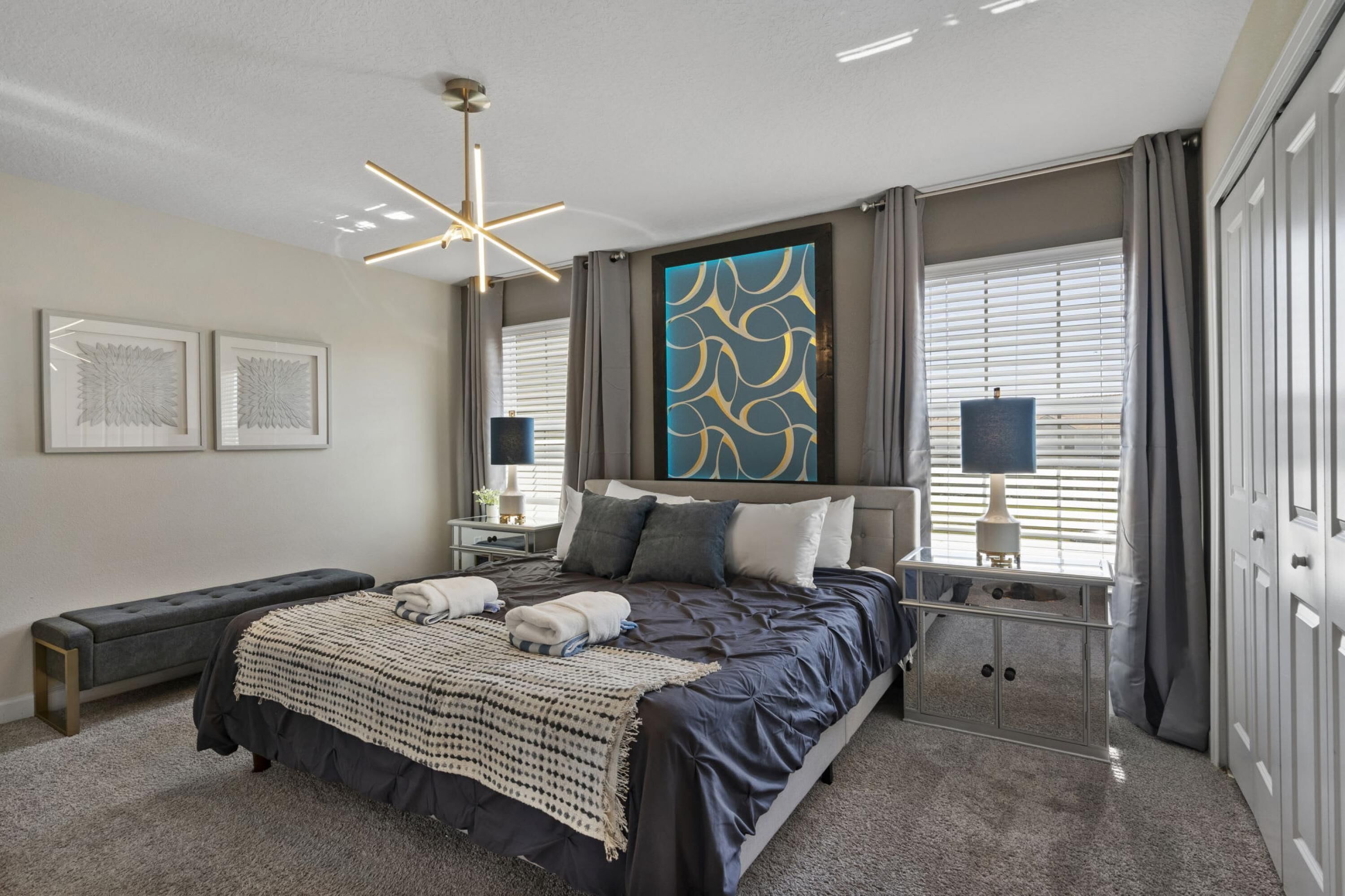 Un dormitorio moderno con una cama grande, mesitas de noche, un banco, una lámpara de techo y un panel decorativo en la pared.